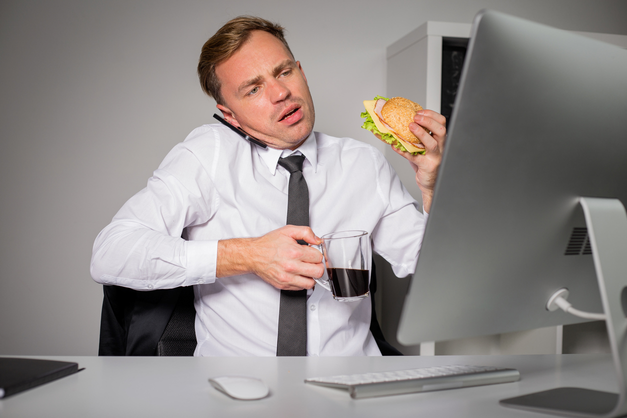 Busy man at the office having coffee and burger