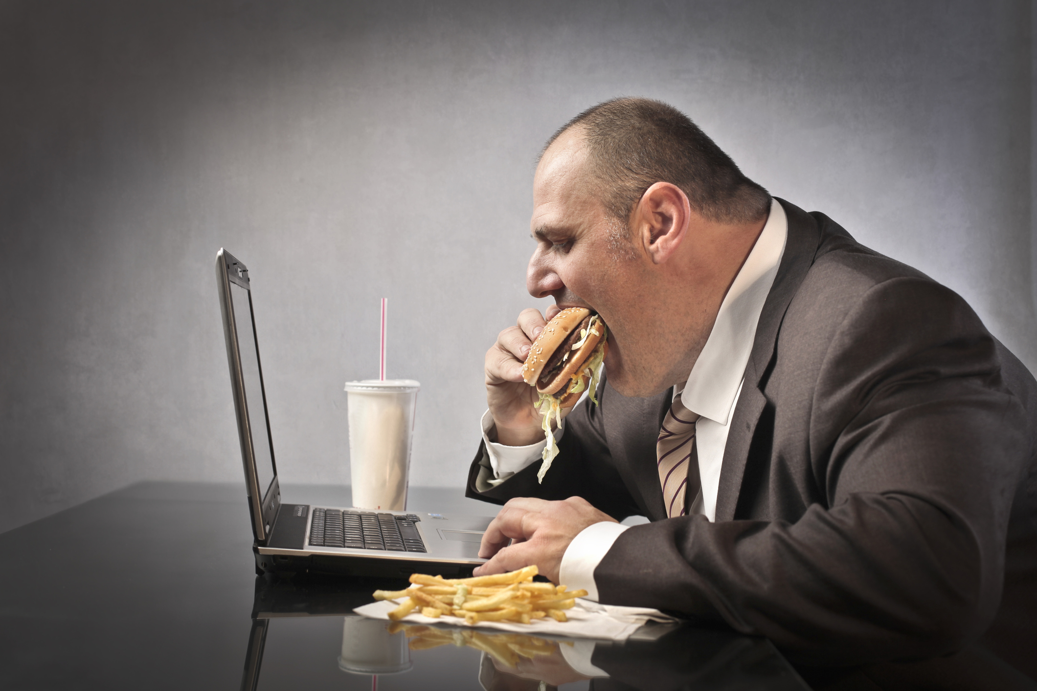 Fat businessman eating junk food in front of a laptop