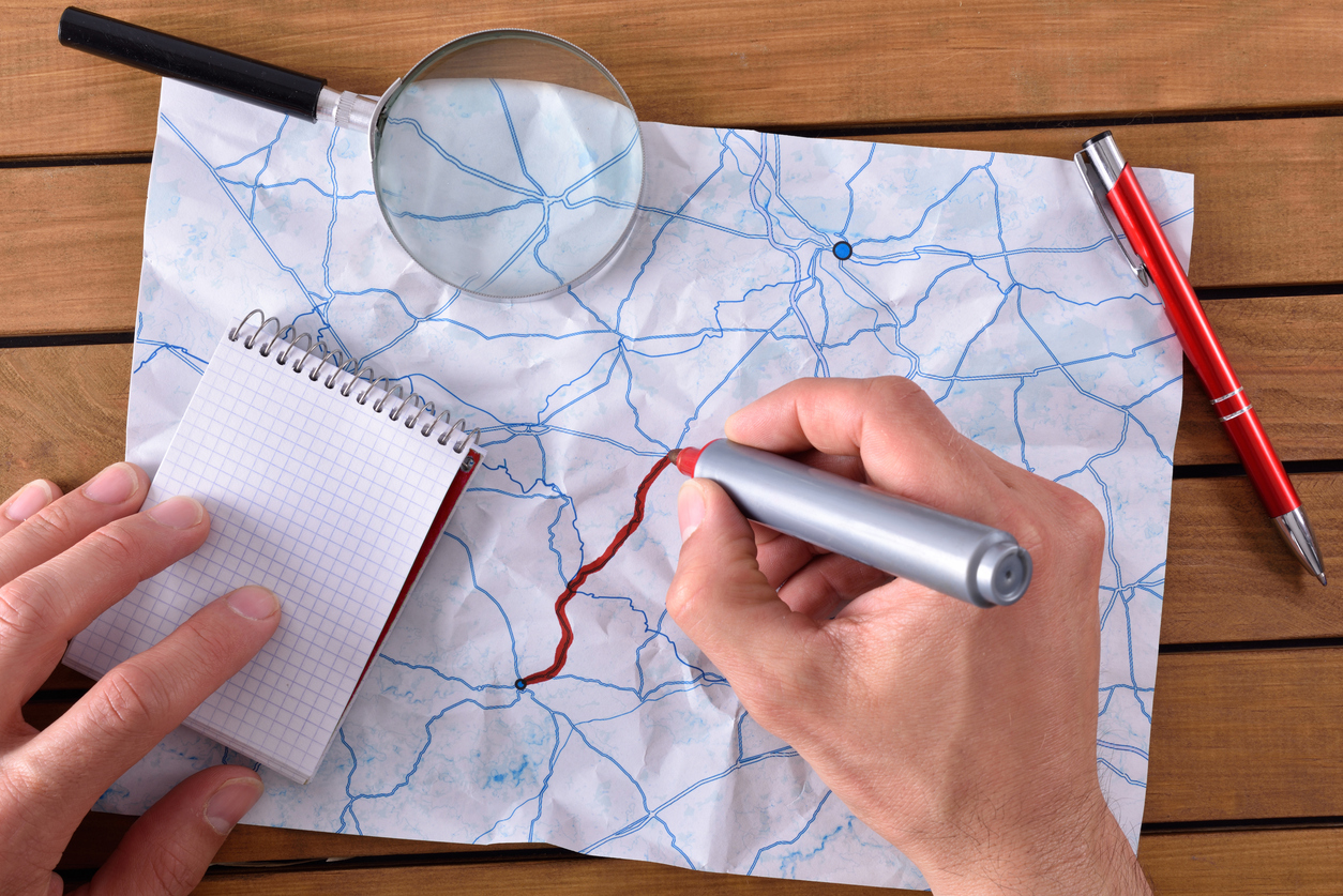 hands tracing a path on map on a wooden table. With pen notepad and magnifying glass. Top view