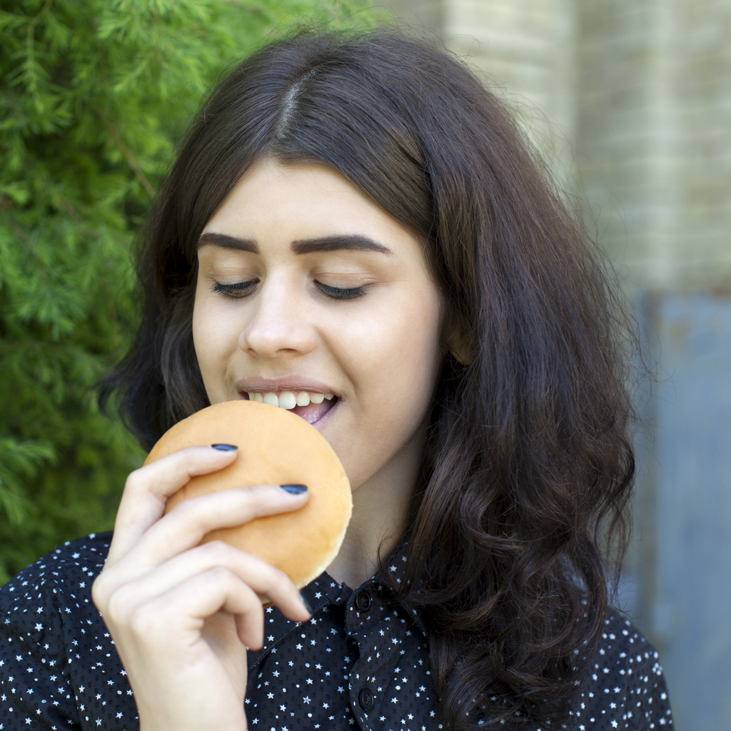 Young girl eat fast food cheeseburger or hamburger on street. Brunette in black shirt